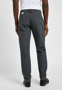 Szare chinosy bawełniane o prostym kroju, z etykietą w pasie i dwiema tylnymi kieszeniami. Noszone z czarnymi butami.