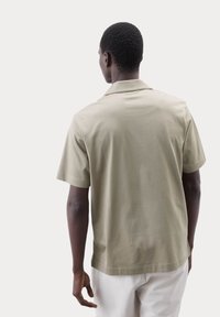Camisa de manga corta en color caqui con un ajuste relajado, que presenta una textura suave y un corte clásico, mostrada desde la parte de atrás.