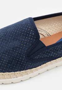 Scarpa slip-on perforata blu navy con parte superiore elastica, suola in stile juta e sottopiede in gomma bianca sottile. L'interno presenta un tessuto di colore chiaro.