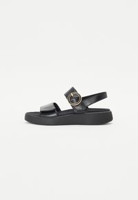 Black leather sandals with a flat platform sole, strap across the instep, and a circular metal accent on the side. Textured detailing on straps.