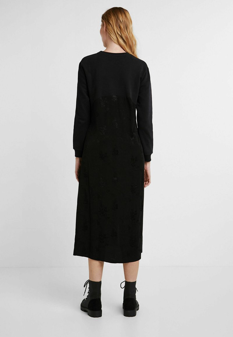 Zwart langharig jurk met een gestructureerde onderzijde met een bloemenpatroon, gecombineerd met zwarte lace-up laarzen voor contrast.