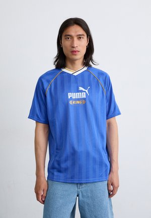 Blå sportstrøje med lodrette striber, hvide accenter og en gul kant. Har et logo og teksten "PUMA KING." Lavet af letvægtsstof.