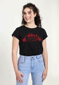 Sort bomulds t-shirt med korte ærmer, der har en rød "MARVEL" grafik. Sammen med højtaljede lyseblå jeans.