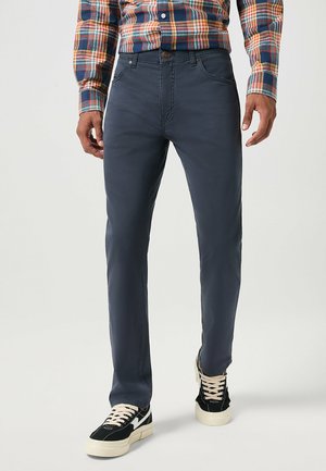Męskie ciemnoniebieskie chinosy, slim fit, wykonane z bawełny, z kieszeniami z przodu, z zapięciem na guzik, stylizowane z czarnymi sneakersami.