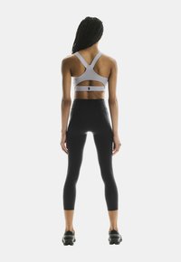 Helles graues Sport-BH mit einem Mesh-Rücken, kombiniert mit hoch taillierten schwarzen Leggings, die seitliche Akzente und strukturierten Stoff aufweisen.