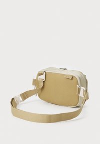 Rechteckige Tasche mit einer strukturierten gelben Außenseite, cremefarbenen Akzenten, verstellbarem Riemen und einem Reißverschluss. Verfügt über seitliche Hardware für Befestigungen.