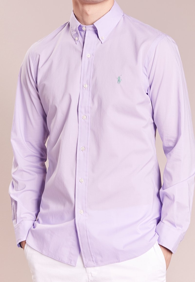 Lila knappkragskjorta med en spetskrage, som har en subtil logotyp och en mjuk, vävd textur. Vita knappar kompletterar designen.