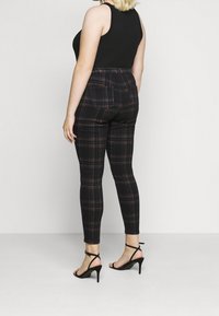 Musta ja punainen ruudullinen trikoo, jossa on korkea vyötärö ja takataskut, yhdistetty mustiin soljillisiin korkokenkiin, nähtynä takaa.