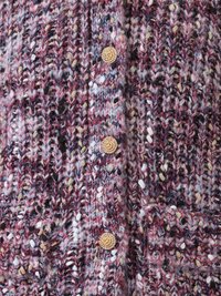 Gestrickte Strickjacke mit einer Mischung aus rotem, lila und cremefarbenem Garn. Goldfarbene Knöpfe auf der Vorderseite und zwei aufgesetzte Taschen mit strukturiertem Design.