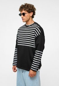 Zwarte lange mouw shirt met horizontale witte strepen op de bovenkant en mouwen. Heeft een relaxte pasvorm en zachte stof. G gedragen met lichte spijkerbroek.