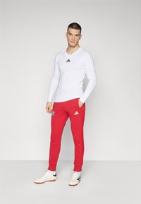 Langermet hvit treningsskjorte med svart logo, kombinert med røde joggebukser med sidestriper og logo-detaljer. Hvite treningssko.