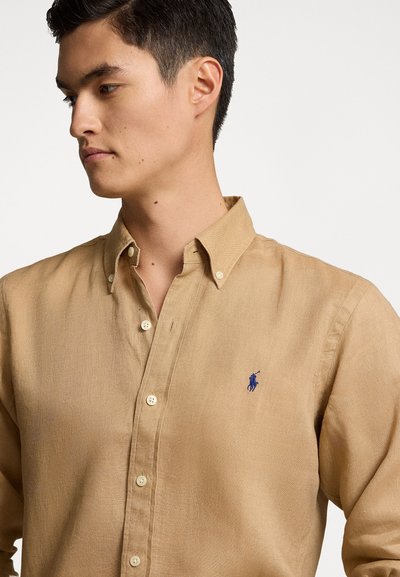 Camicia button-down beige chiaro realizzata in un tessuto testurizzato. Presenta un piccolo logo ricamato blu sul lato sinistro del petto e un classico design del colletto.