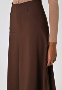 I pantaloni marroni a gamba larga presentano una texture liscia, tasche laterali e una chiusura con bottone frontale, con una vita aderente e una silhouette fluida.