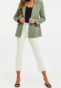 Blaser vert clair avec des revers à cran et une fermeture à un bouton, associé à un jean blanc court avec des ourlets effilochés et des talons ouverts noirs.