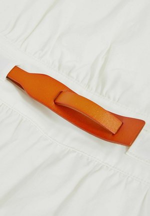 Valge kangas, millel on kogutud tekstuur, esitades silmapaistvat oranži nahkrihma. Rihmal on sile viimistlus ja lame disain.