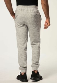 Grå sweatpants med et tekstureret mønster, elastisk talje, ribbede manchetter og baglomme. Sammen med sorte sportssko.