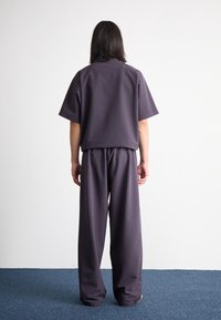 Volný, tmavě šedý dvoudílný outfit se krátkým rukávem a širokými kalhotami, vyrobený z hladkého materiálu s čistým designem.