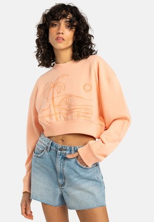 Sweatshirt cropped de couleur pêche avec broderie d'un palmier et d'un soleil, associé à un short en denim bleu clair avec un ourlet effiloché et des poches avant.
