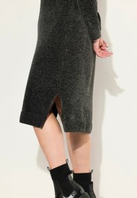 Robe en tricot gray avec un ourlet côtelé, des fentes latérales et une finition texturée. Associée à des bottines noires avec des poignets côtelés.