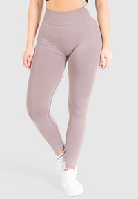 Leggings a vita alta in un leggero color malva, realizzati in materiale elasticizzato, con una texture liscia e dettagli nei pannelli laterali. Indossati con sneakers bianche.