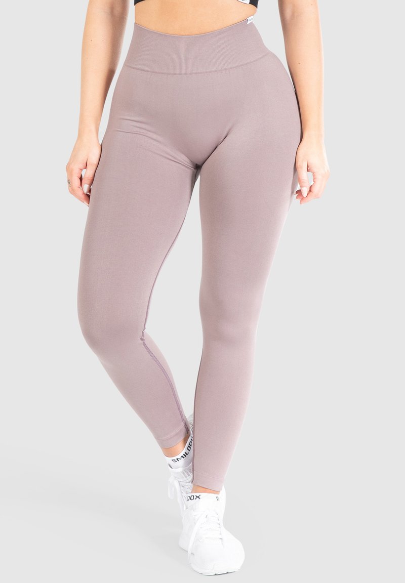 Leggings a vita alta in un leggero color malva, realizzati in materiale elasticizzato, con una texture liscia e dettagli nei pannelli laterali. Indossati con sneakers bianche.