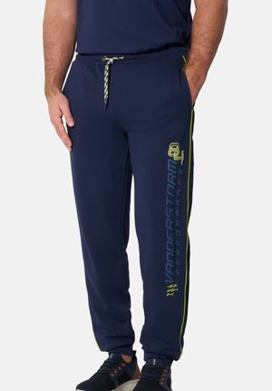 Man wearing navy blue joggers with yellow side stripes and "Vanderstorm Performance" text on left leg, paired with black athletic shoes.