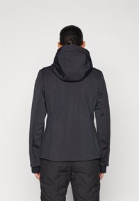 Zwarte softshell jas met een capuchon, aangesloten ontwerp en getextureerde manchetten, gedragen over donkere broeken, met een gladde buitenkant en zonder zichtbare sluitingen.
