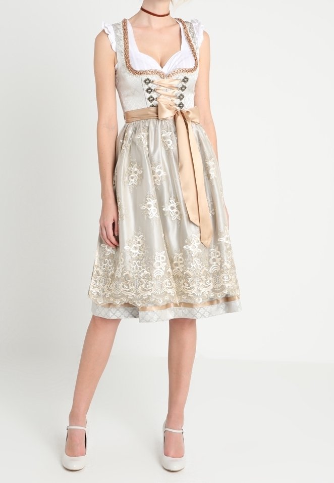 Robe traditionnelle avec un corsage en dentelle blanche et une jupe beige ornée de broderies florales, ceinture en satin, et des talons fermés blancs.