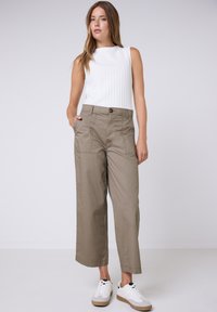 Top bianco senza maniche leggero con texture a coste, abbinato a pantaloni khaki a gamba larga con tasche frontali e chiusura a bottone. Sneaker bianche.