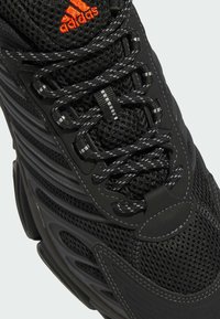 Baskets Adidas noires en tissu mesh, lacets réfléchissants noirs et blancs, et logo Adidas orange vif sur la languette.