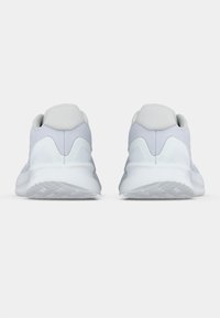 Een paar lichtgrijze sport sneakers gezien vanaf de achterkant op een effen witte achtergrond, waarbij de textuur van de zolen en het ontwerp van de hak wordt benadrukt.