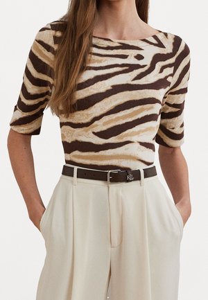 Vrouw die een beige en bruine zebraprint top draagt met ellebooglange mouwen, ingestopt in een high-waist crème broek en een donkerbruine riem.