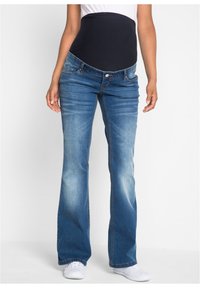 Jeans a zampa d'elefante in denim blu con un cinturino elastico scuro, dotati di tasche frontali e di un leggero effetto di lavaggio sbiadito. Indossati con sneakers bianche.
