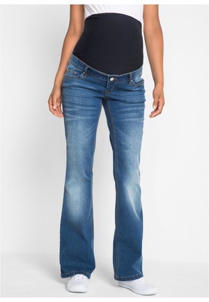 Jeans a zampa d'elefante in denim blu con un cinturino elastico scuro, dotati di tasche frontali e di un leggero effetto di lavaggio sbiadito. Indossati con sneakers bianche.