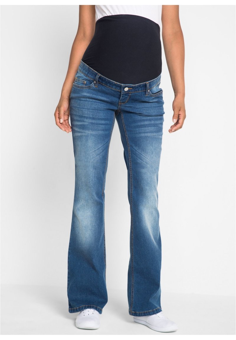 Jeans a zampa d'elefante in denim blu con un cinturino elastico scuro, dotati di tasche frontali e di un leggero effetto di lavaggio sbiadito. Indossati con sneakers bianche.