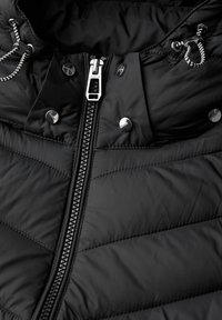 Svart vadderad jacka med silverfärgad dragkedja, tryckknappar och huva med justerbara snoddar. Tyget har en slät textur.