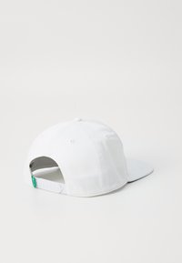 Hvit baseballcaps med flat skygge, laget av bomull. Har en justerbar plaststropp bak og en liten grønn logo på siden.