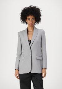 Grå skraddersydd blazer med notert krage, to frontknapper og klafflommer. Har subtil tekstur og strukturert passform.