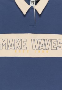 Námornícka modrá polo košeľa s krémovým golierom, so všitým nápisom "MAKE WAVES" a "ROXY 1990". Voľný strih, bavlnený materiál.