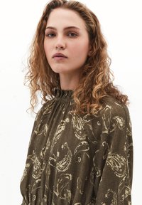 Blouse à motifs marron avec un col haut, des manches longues et un design fluide, ornée d'un imprimé cachemire aux teintes douces.