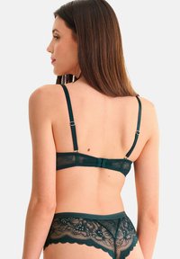 Soutien-gorge en dentelle vert foncé avec des bretelles réglables, décoré de motifs floraux et doté d'une fermeture à crochets à l'arrière. Associé à des sous-vêtements en dentelle assortis.