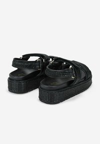 Sandalias de plataforma negras con correas de tejido trenzado, plantilla acolchada y suela texturada. Cuenta con correas ajustables en el tobillo y acentos de herrajes dorados.