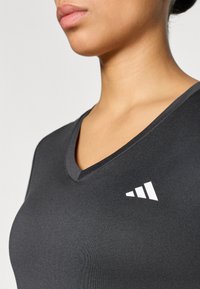 Czarny sportowy top z dekoltem w serek o dopasowanym kroju, z wyraźnym białym logo na piersi. Gładka faktura i lekka tkanina.