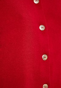 Cardigan rosso in maglia con trama a coste e bottoni tono argento lungo la parte anteriore, evidenziando elementi di design pratici e puliti.