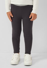 Leggings noirs en tissu extensible, dotés d'un design ajusté. Associés à des baskets blanches, présentant une semelle plate et un laçage à l'avant.