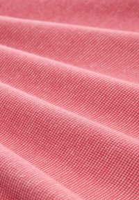 Tissu en coton rose clair avec un motif texturé, affichant de fines lignes diagonales et une subtile brillance, drapé en douces plis.