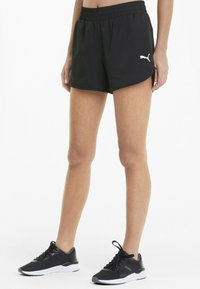 Schwarze Sportshorts mit einem elastischen Bund, mit einem kleinen weißen Puma-Logo. Kombiniert mit schwarzen Trainern und weißen Sohlen.