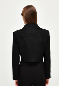 Czarna krótka kurtka z wyłamaną kołnierzem, wyraźnymi ramionami i widocznymi szwami. Gładka faktura i elegancki design.