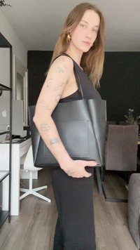 Černá kožená taška přes rameno se strukturovaným designem, obsahující přední kapsu a zaoblené horní okraje. Hladký povrch a minimalistická estetika.