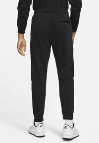 Musta urheiluhaalari, jossa on joustava vyötärö ja kootut nilkat, sisältäen takataskun. Yhdistettynä valkoisiin tennareihin. Sileä kankaan rakenne.